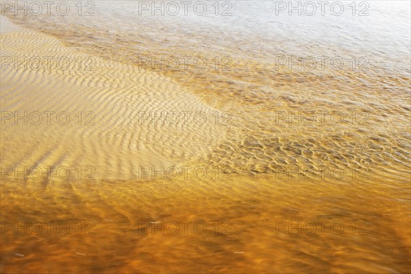 Reddish ferruginous water flows over a sandy beach at low tide