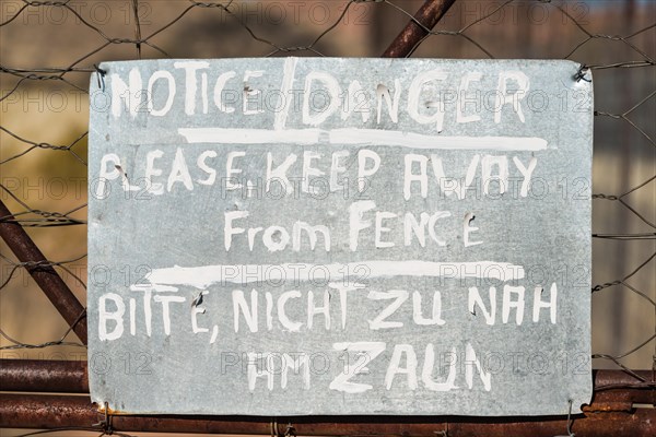 Warning sign in English and German on the fence of a predator enclosure