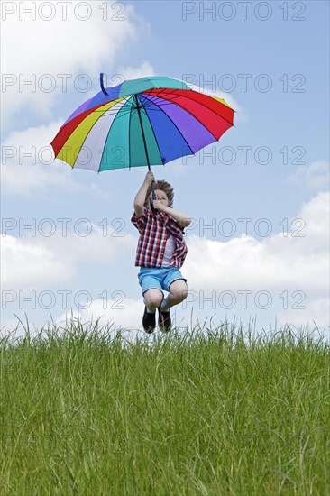 Boy with colorful umbrella jumping on meadow