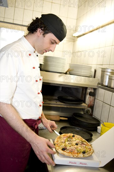 Pizza baker putting a pizza in a pizza box