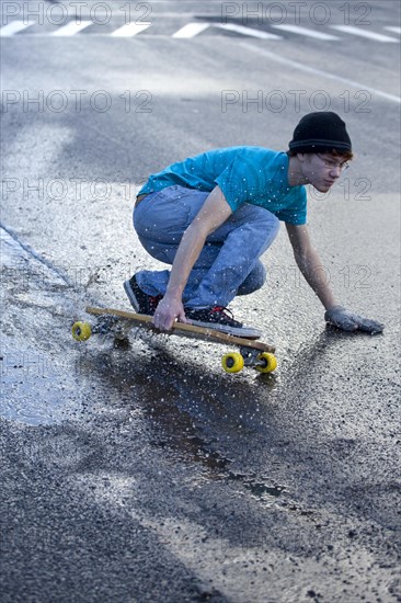 Teenager riding a longboard downhill on a wet street