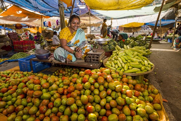 A woman is selling tomatoes and cucumbers at the weekly vegetable market