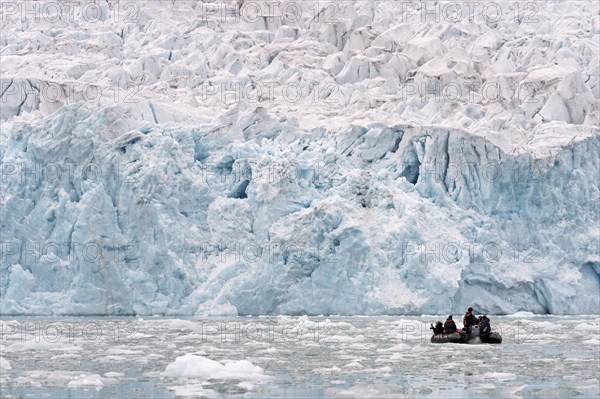 Tourists in a rubber dinghy in front of the rim of the Monacobreen Glacier