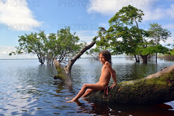 Girl sitting on a tree trunk of a giant rainforest tree on the banks of the Amazon and Rio Solimoes
