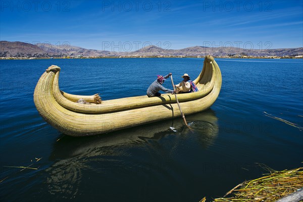 Two local people rowing a traditional boat made of totora reeds on Lake Titicaca