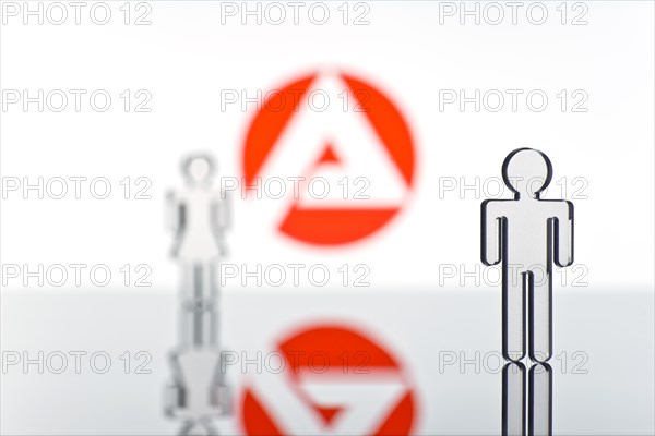 Two figures standing in front of the logo of the German employment agency