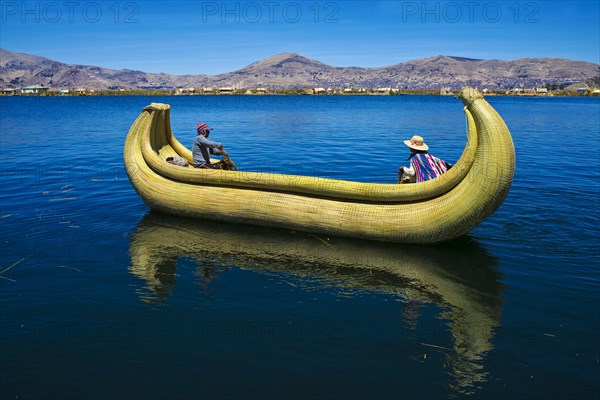 Two local people rowing a traditional boat made of totora reeds on Lake Titicaca