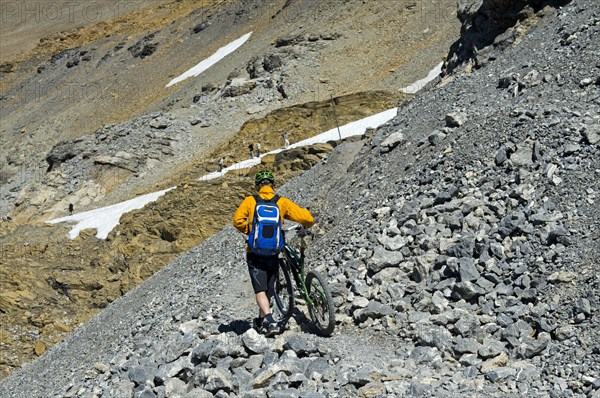 Mountain biker pushing his bike on a single trail in rocky terrain