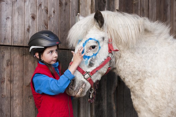 Girl wearing a riding helmet painting a pony with finger paints