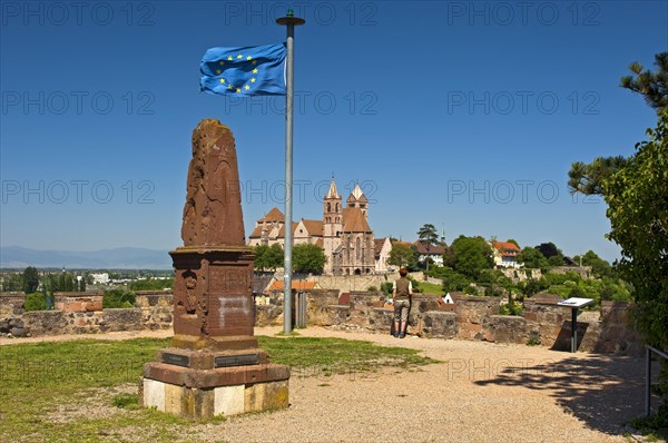 Obelisk and the European flag on Eckartsberg hill in front of the historic centre of Breisach with St. Stephansmunster Cathedral