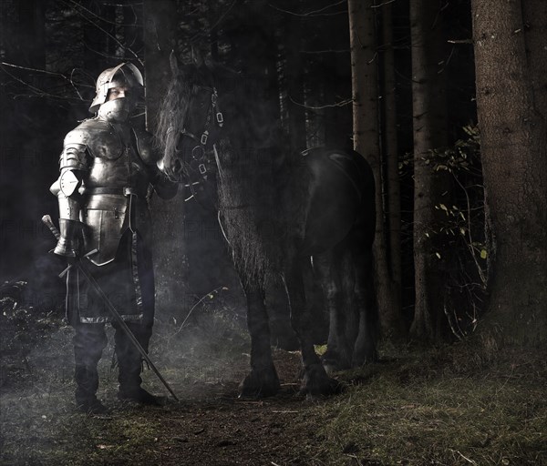 Knight wearing armour standing beside his horse in the woods