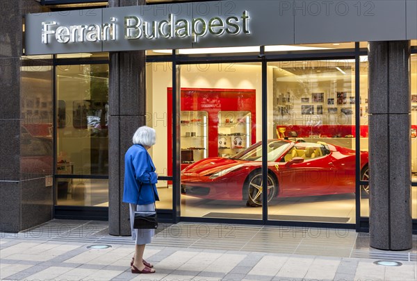 Elderly woman standing in front of the shop window of a Ferrari dealer