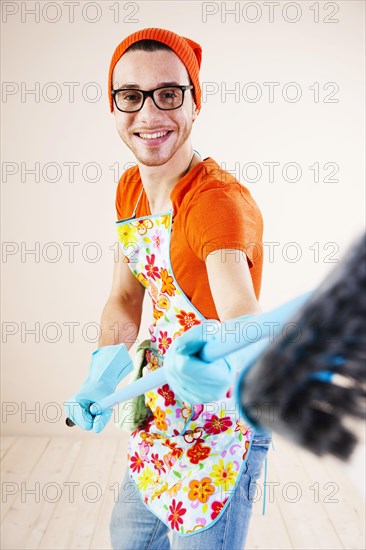 Young man wearing an apron and cleaning gloves holding a broom