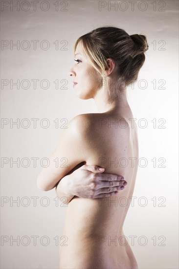 Naked young woman standing with her arms folded