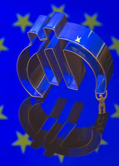Miniature figure of a worker is carrying the Euro-symbol