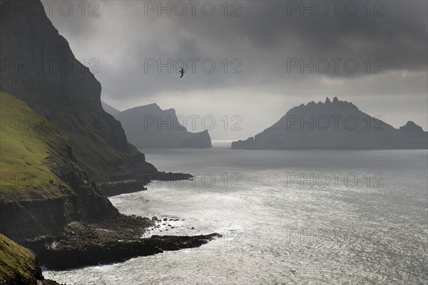 Cliffs in front of the silhouette of the rugged rocks of Tindholmur