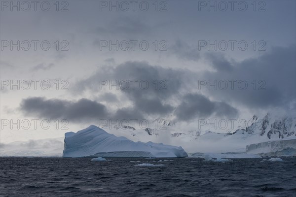Iceberg in a fjord with mountain scenery and a cloudy sky