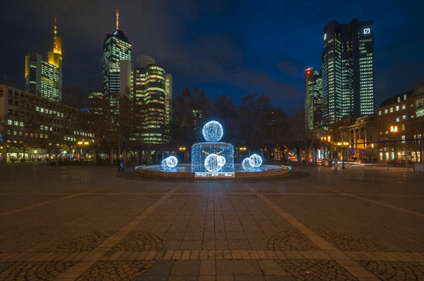 Illuminated Lucae Fountain on Opernplatz square in front of illuminated high-rise skyline