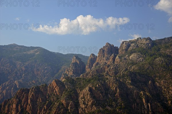 The typical rocky mountains of western Corsica near Evisa below a blue sky with a lone white cloud. Evisa illuminated by warm evening light surrounded by mountains. Evisa is in the department Corse-du...