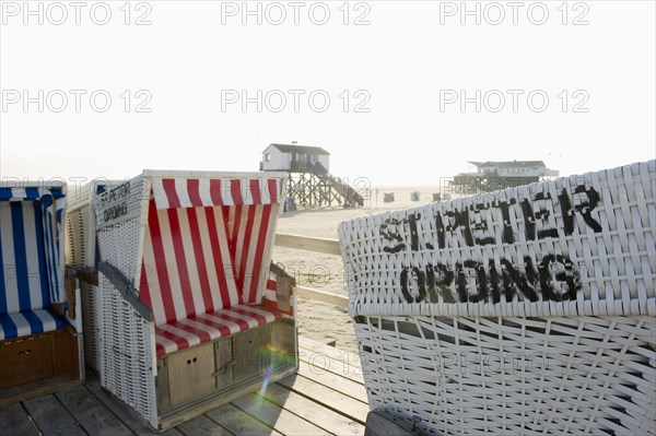 Roofed wicker beach chairs on the beach in front of houses on stilts