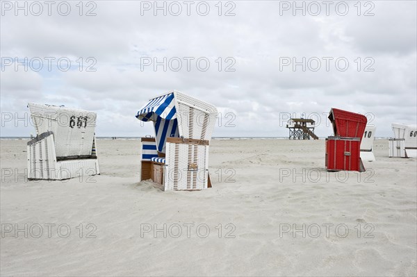 Roofed wicker beach chairs on the beach in front of a house on stilts