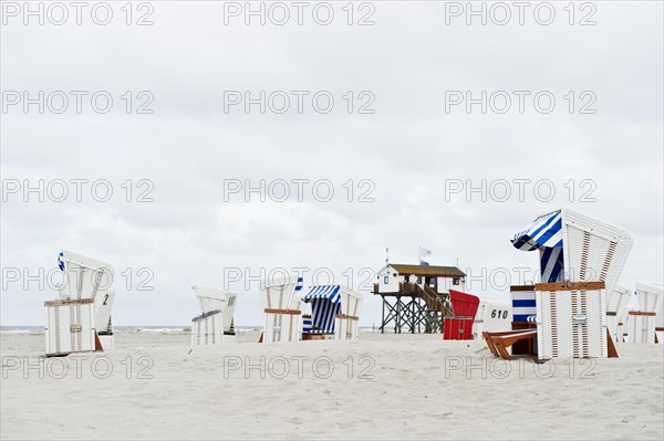 Roofed wicker beach chairs on the beach in front of a house on stilts