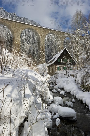 Snow-covered creek with a Black Forest house and a railway bridge