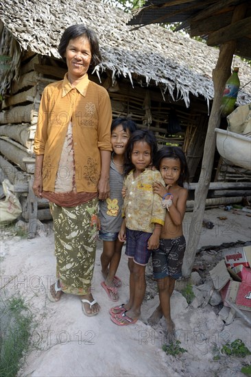 Woman standing with three girls in front of a hut made of wood and straw