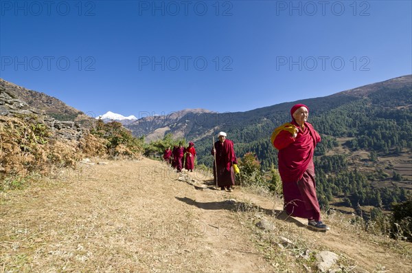 Monks and nuns wearing red cloths walking on a small path along a mountain slope