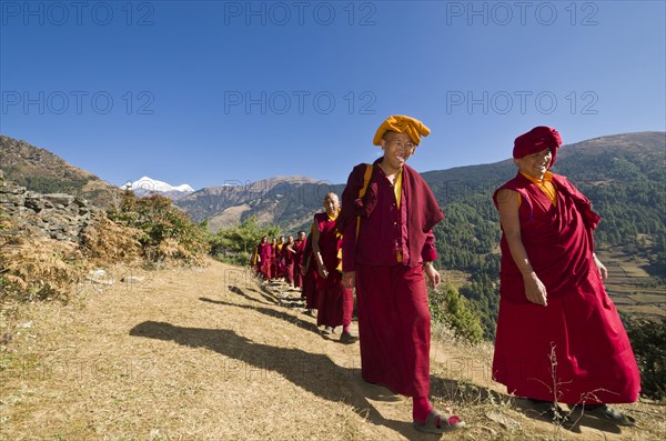 Monks and nuns wearing red cloths walking on a small path along a mountain slope