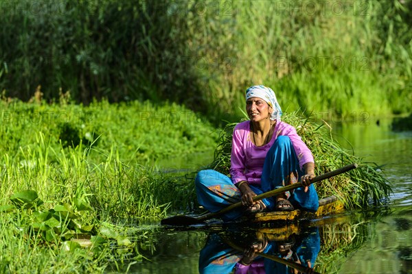 A woman paddeling in a shikara boat on a canal near Dal Lake