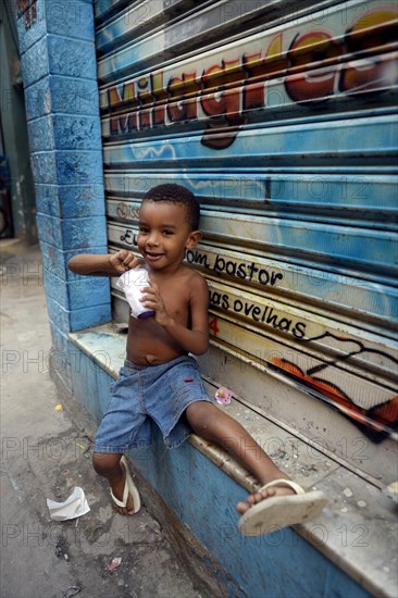 Boy eating from a tub of ice cream in a slum or favela