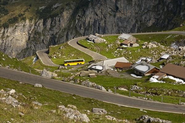 Yellow bus from the PostAuto Schweiz AG in a hamlet on the serpentine-rich Klausen Pass road