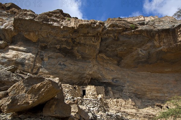 Stone huts of the abandoned settlement of Sap Bani Khamis under a ledge in the Grand Canyon of Oman in the Wadi at Nakhar