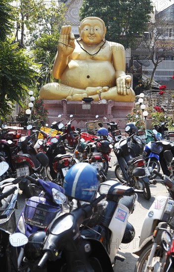 Parking lot for motor scooters in front of a large golden Buddha statue