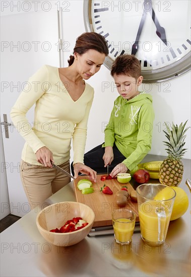 Mother and son cutting various kinds of fruit on cutting board in a kitchen