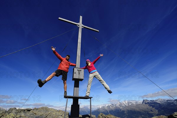 Hikers on the summit cross on the summit of Boeses Weibele Mountain in the Defregger Group