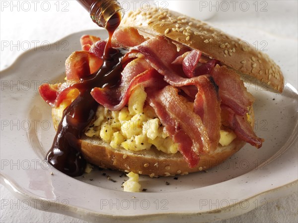 Crispy streaky bacon and scrambled eggs on a bagel with brown sauce