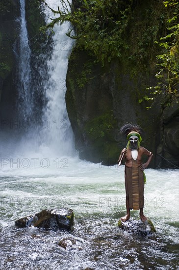 Decorated and painted tribal chief standing in front of a waterfall in the Highlands