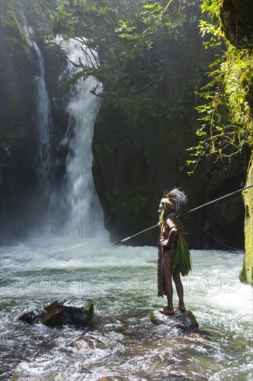 Decorated and painted tribal chief standing in front of a waterfall in the Highlands