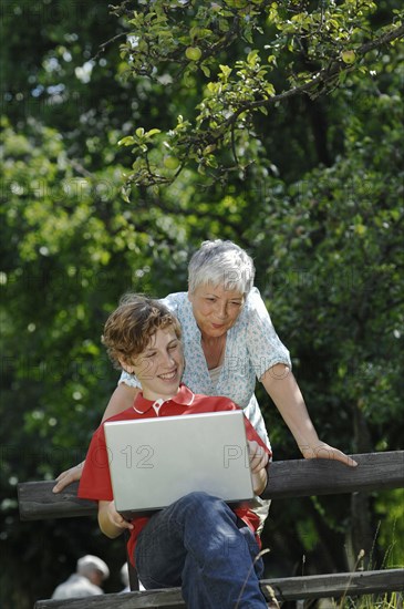 Grandson and grandmother looking together at a laptop computer on a park bench