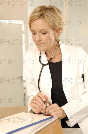 A female doctor in a white coat with stethoscope is standing at a reception desk
