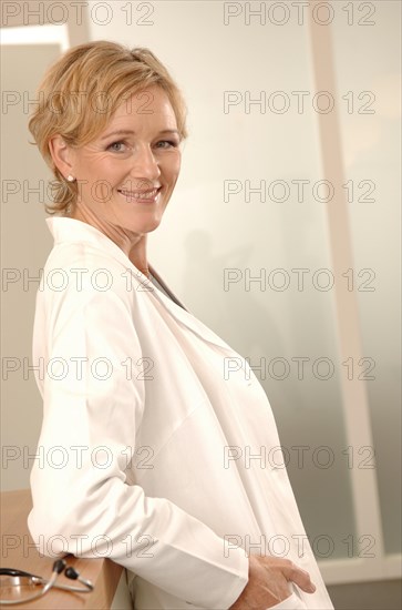 A female doctor in a white coat is standing at a reception desk