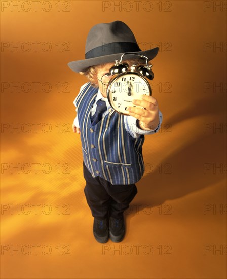 Boy wearing business clothes holding an alarm clock showing eleven fifty-five