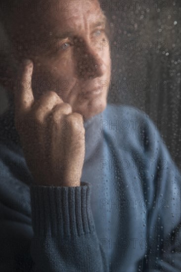 Lonely man sitting behind a window covered in rain drops