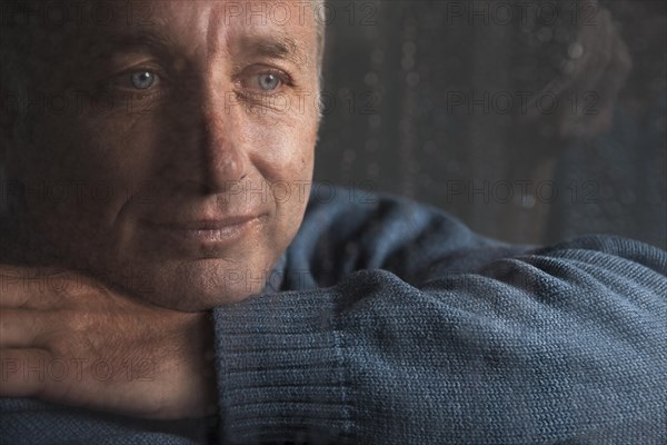 Lonely man sitting behind a window covered in rain drops