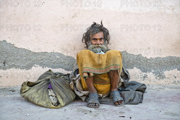 Beggar leaning against a house wall