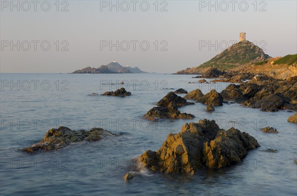 The genoese tower Tour de la Parata at the right and the islands Les Iles Sanguinaires behind the rocky mediterranean coast illuminated by warm morning light. Les Iles Sanguinaires are in the departme...