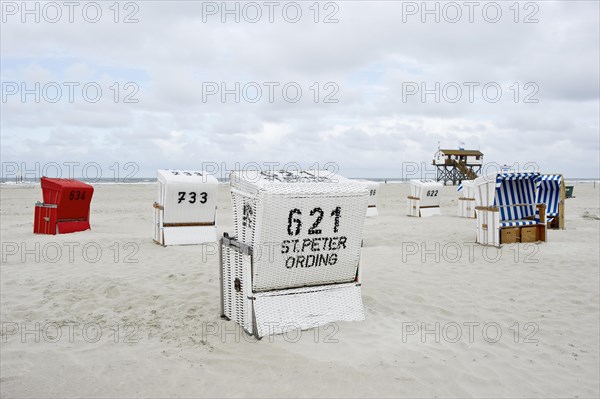 Roofed wicker beach chairs on the beach in front of a house on stilts