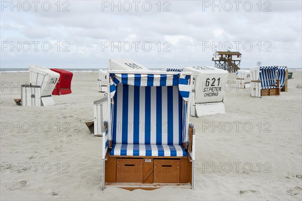 Roofed wicker beach chairs on the beach in front of a house on stilts